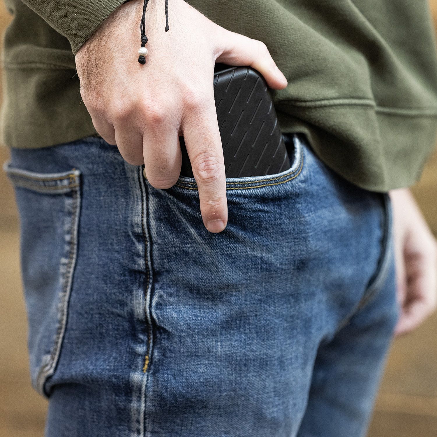 Harrows Slimcase Dart Case Eine Person steckt ein schwarzes Etui in die Hosentasche. Sie trägt eine grüne Jacke und eine blaue Jeans.