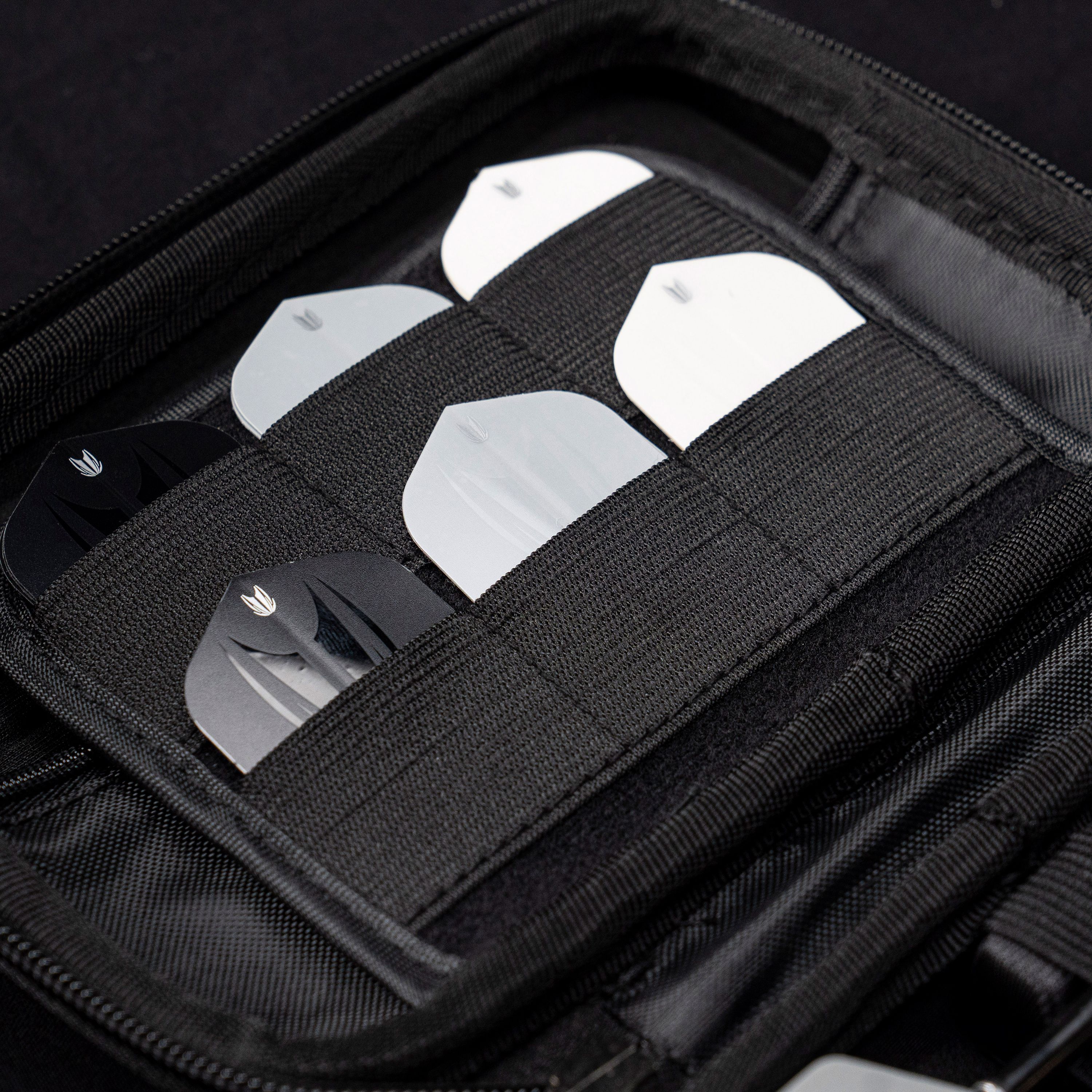 Target Takoma Luke Littler XL dart case Das Bild zeigt das „Target Takoma Bolide XL Dartcase“, das mehrere Dart-Flights in schwarzen und weißen Farben organisiert aufbewahrt. Die Flights sind sicher in elastischen Halterungen im Inneren des schwarzen Etuis verstaut.